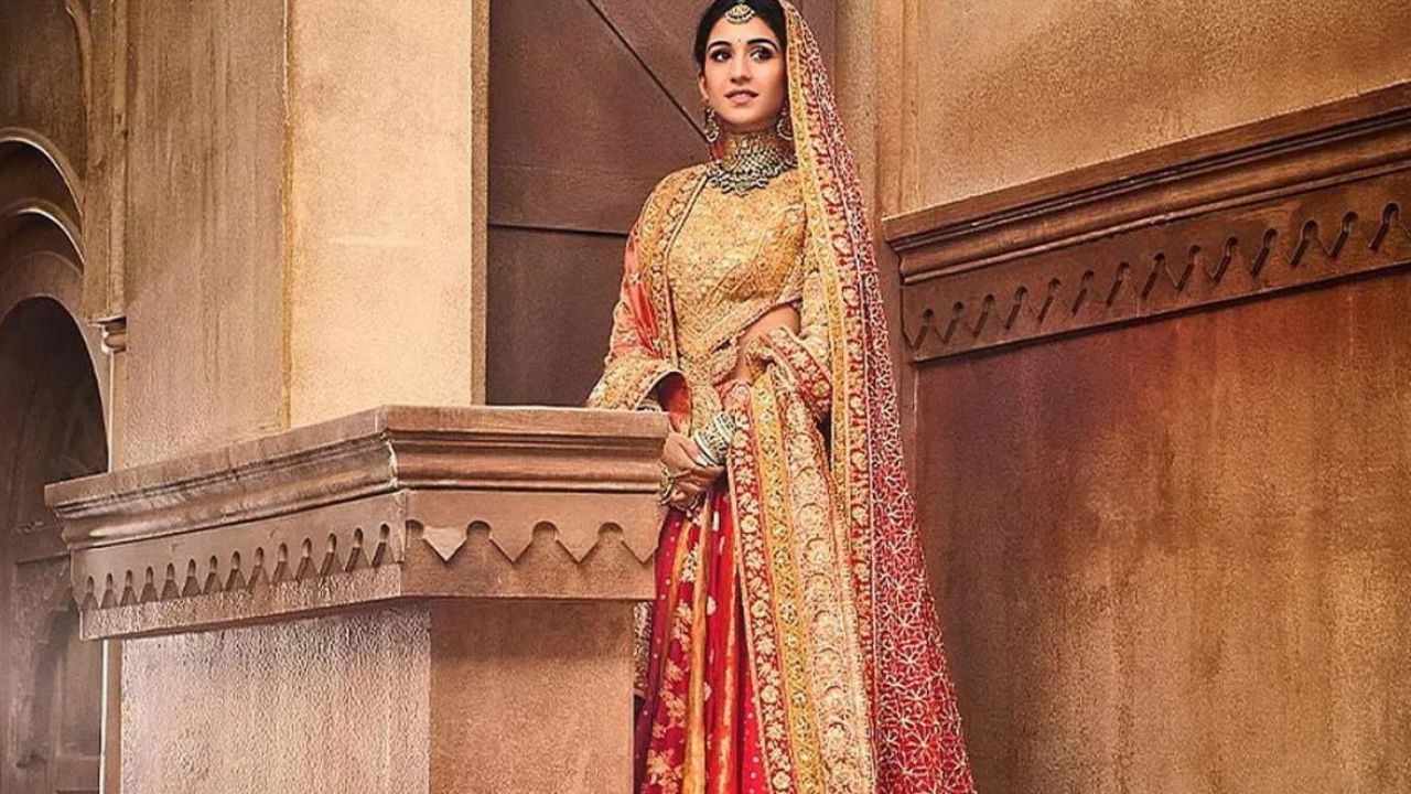 Radhika Merchant wedding pics:চিণ্ডুৰী ৰঙা ৰঙৰ বহু পেনেলযুক্ত বানাৰসী লেহেংগাৰ সৈতে আছিল পৰম্পৰাগত আভো আৰু প্ৰকৃত সোণৰ কাৰ্চোবি কৰা ব্লাউজ।