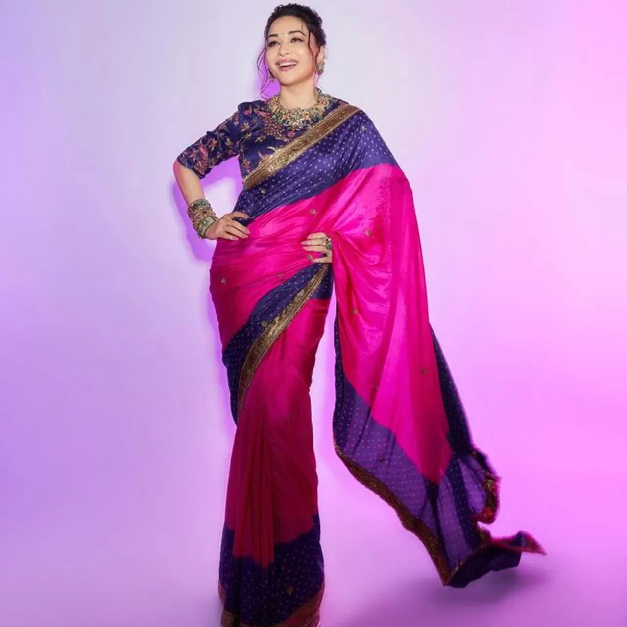 ইয়াত মাধুৰী দীক্ষিতে নীলা আৰু গুলপীয়া ৰঙৰ বান্ধনী ৰেচম শাৰীৰ সৈতে জৰি এম্ব্ৰইডাৰীৰ ব্লাউজ পিন্ধিছে। তেওঁইৰ শাৰীখনৰ বৰ্ডাৰ সোণালী লেচেৰে ডিজাইন কৰা হৈছে। এই শাৰী লুকটোও ৰাখীৰ বাবেও উপযুক্ত।