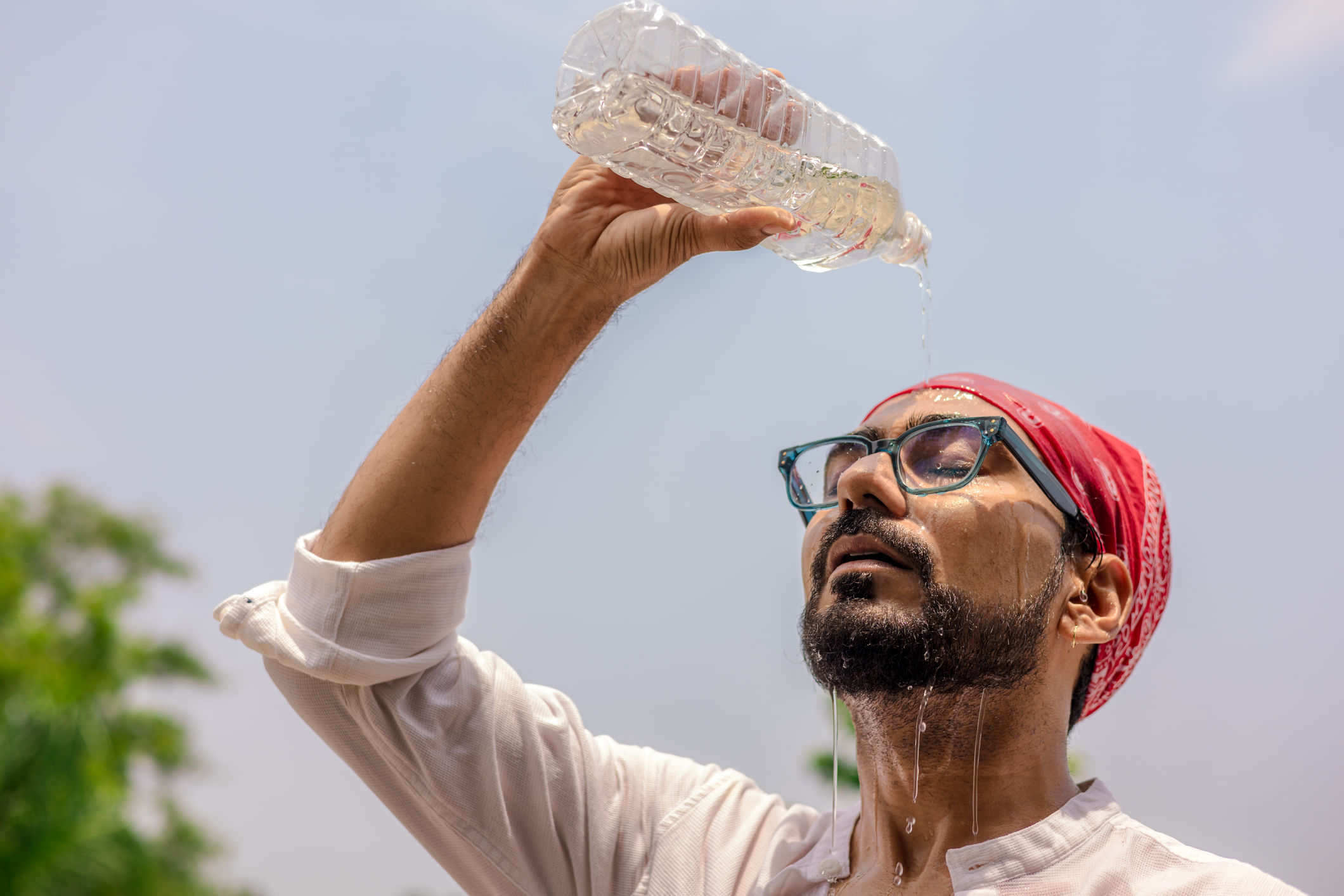Heat Wave: A Close Up Of A Young Man Pouring Water From A Plastic Bottle On His Face During A Hot Afternoon While Traveling.